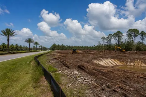 Two machines working a multi-acre commercial clearing along a Palm Coast parkway with mulch windrows and silt fence at the perimeter